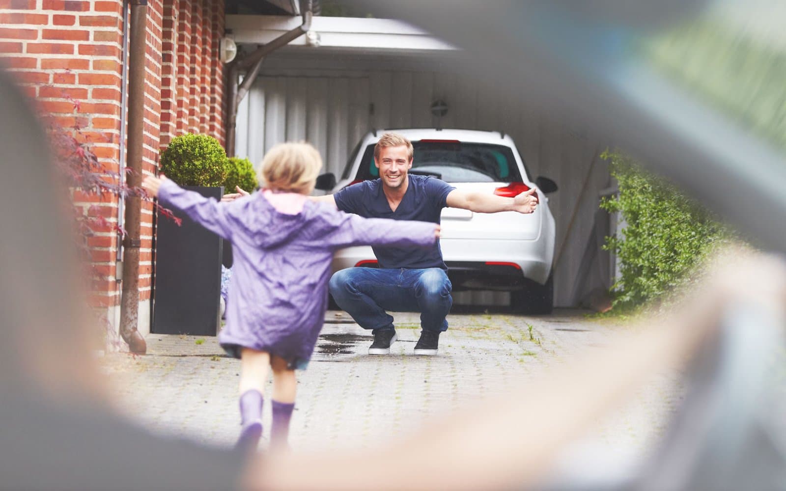 Kind läuft dem Vater vor dem Haus mit offenen Armen entgegen